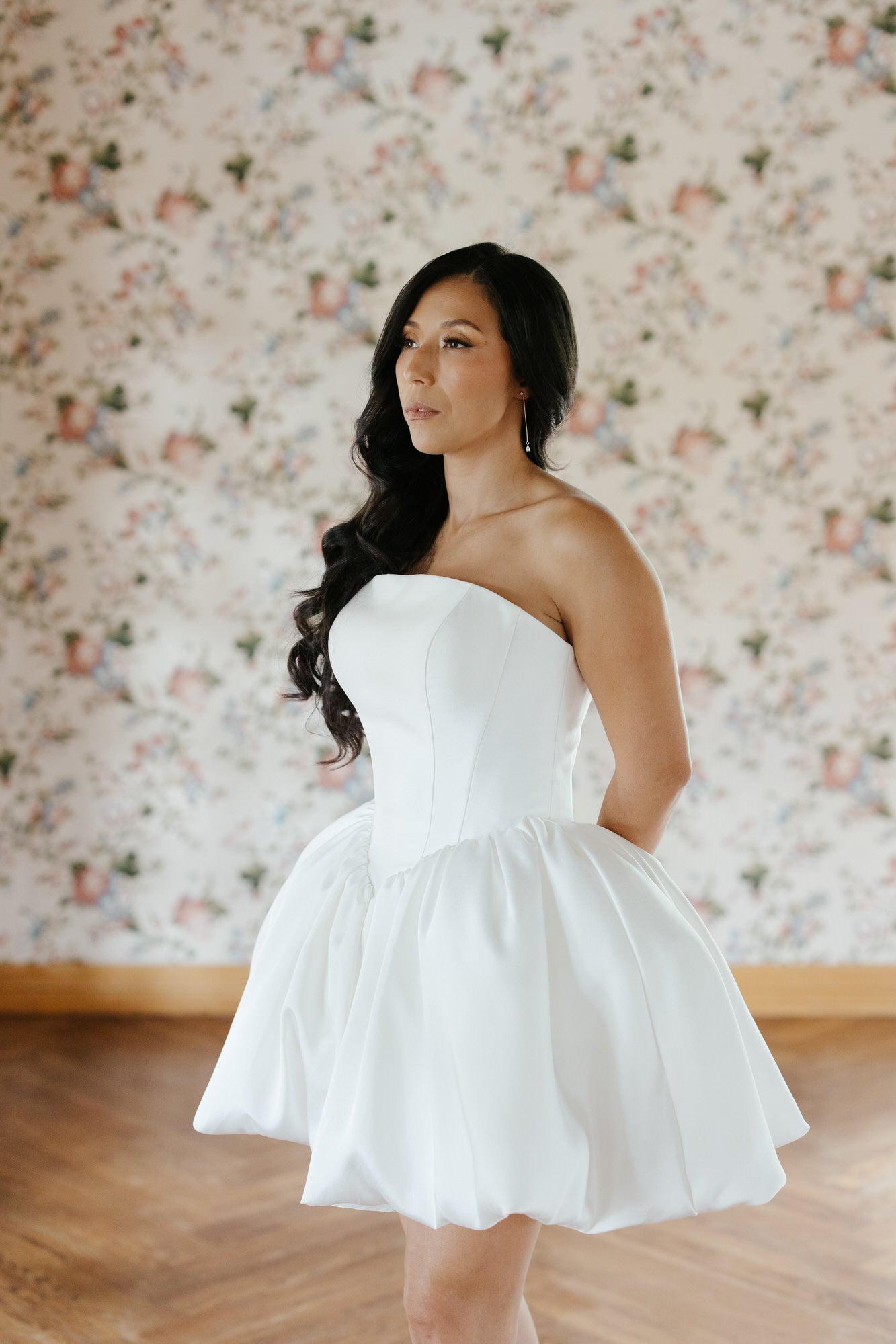 Woman wearing a white strapless dress against a floral wallpaper background