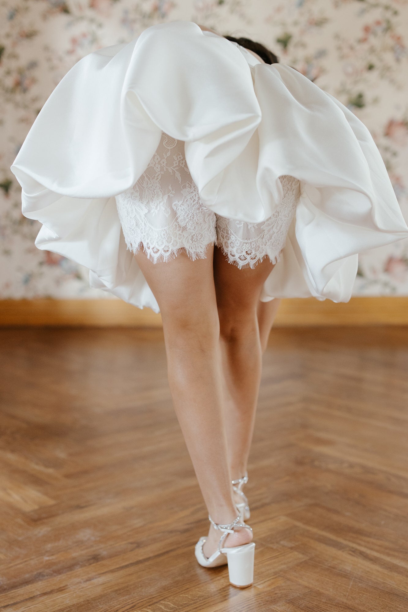Person wearing a white lace dress with a flowing skirt on a wooden floor.
