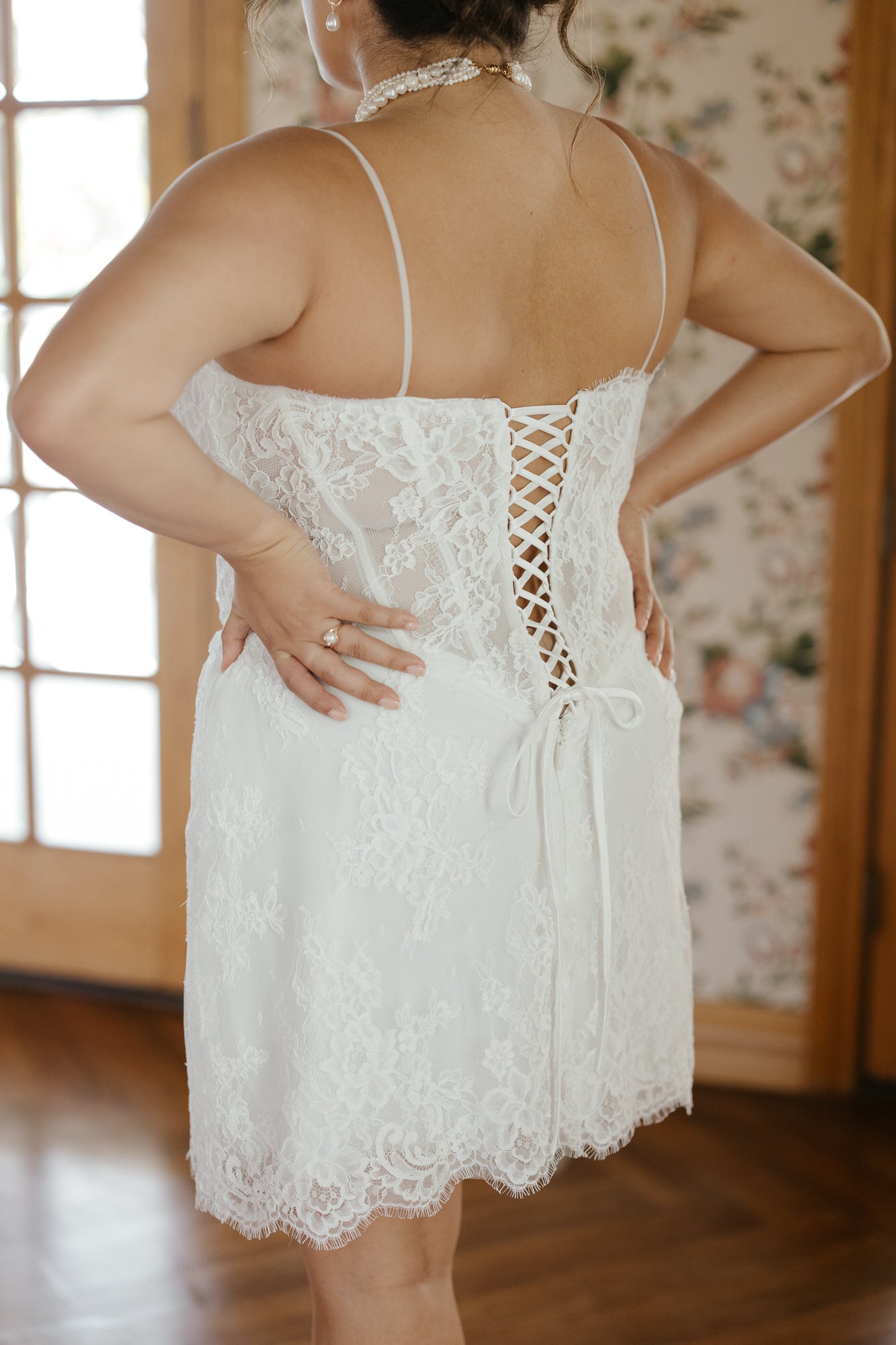 White lace dress with a floral patterned wall in the background
