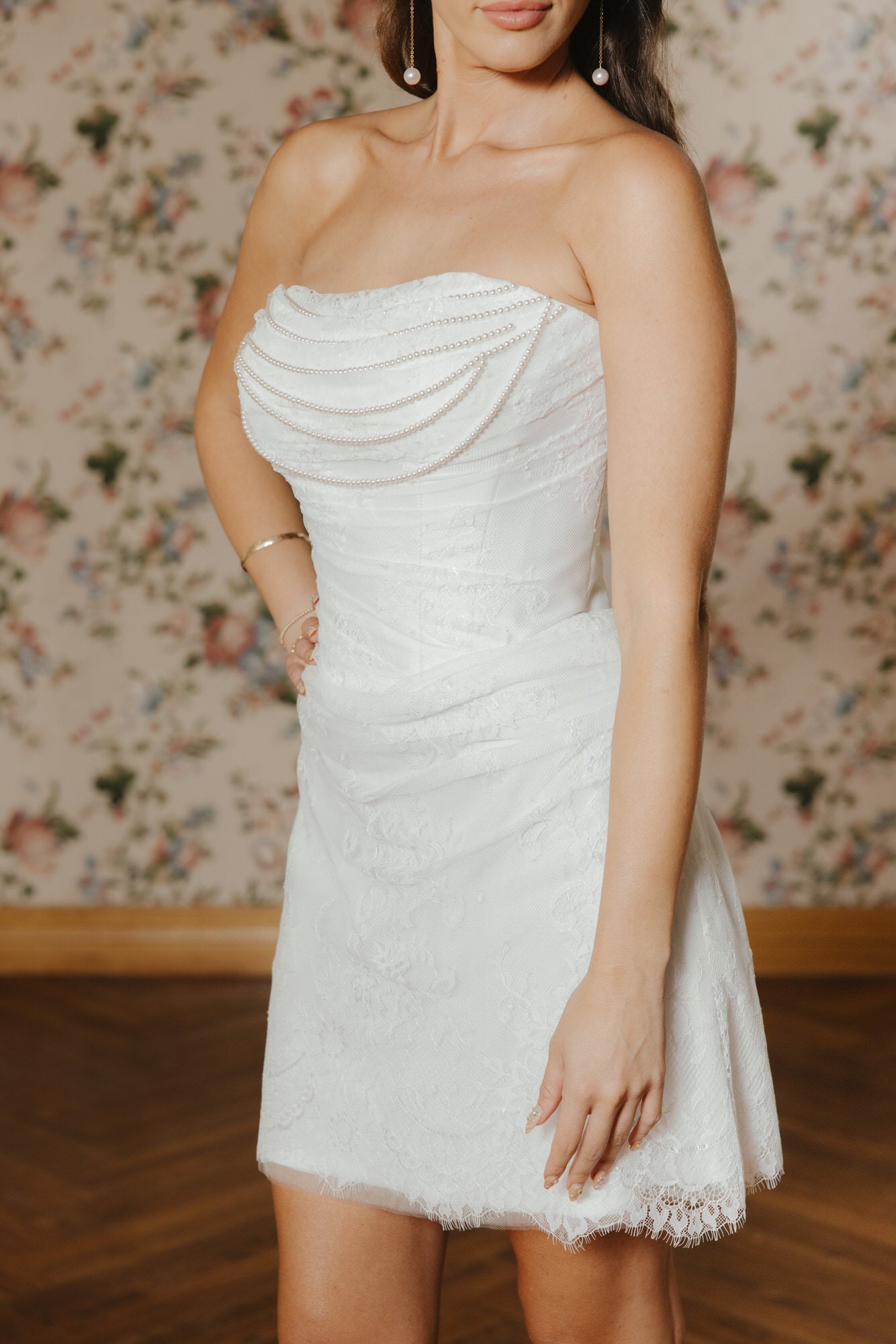 Woman wearing a strapless white dress with floral wallpaper in the background