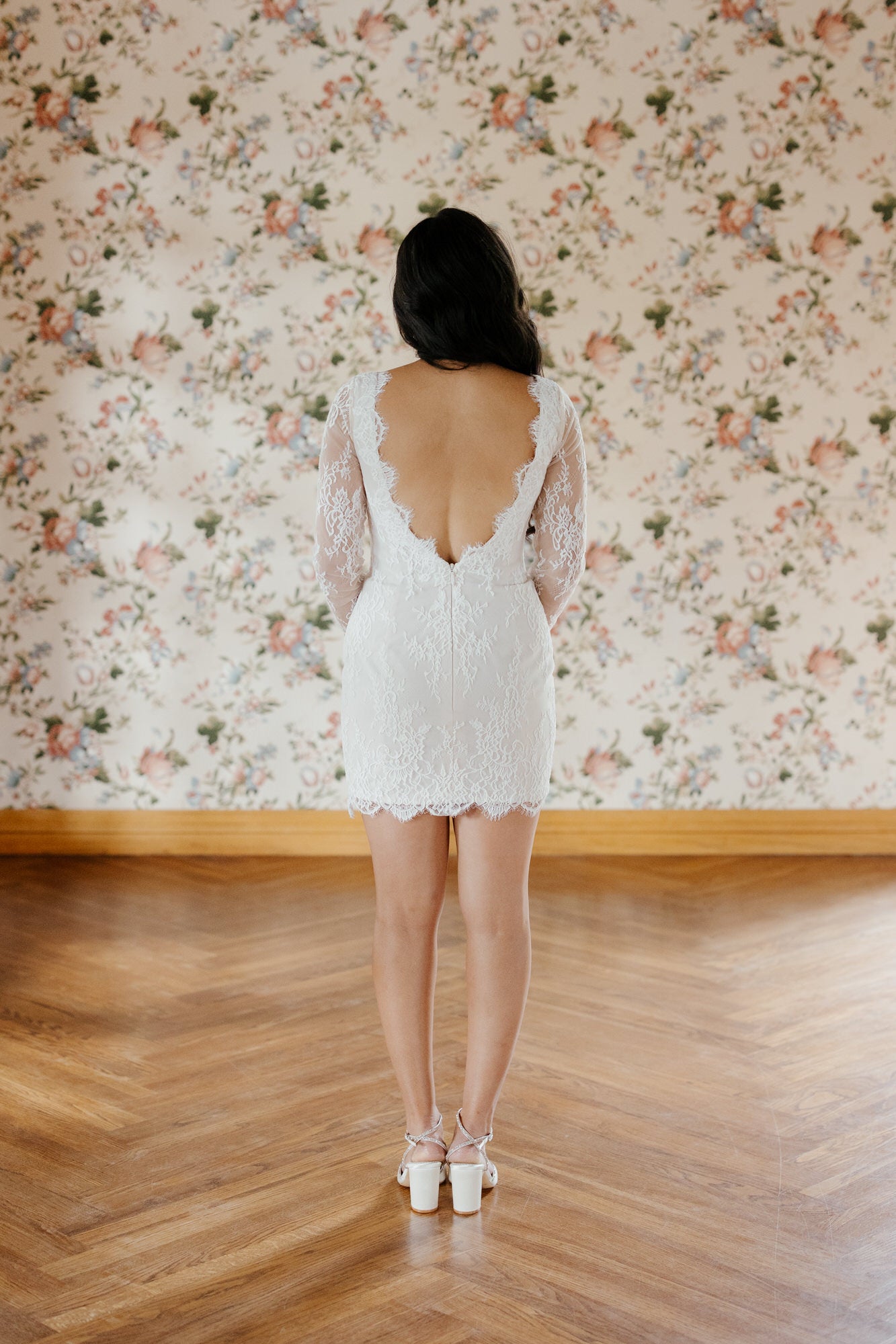 Woman wearing a white lace dress with a floral wallpaper background