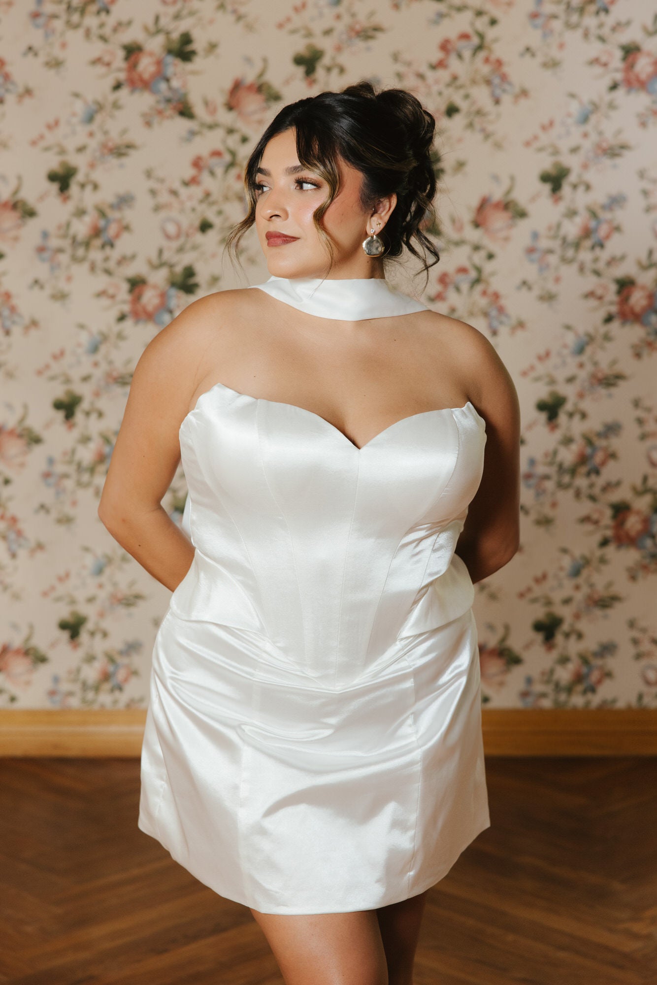 Woman wearing a white dress against a floral wallpaper background