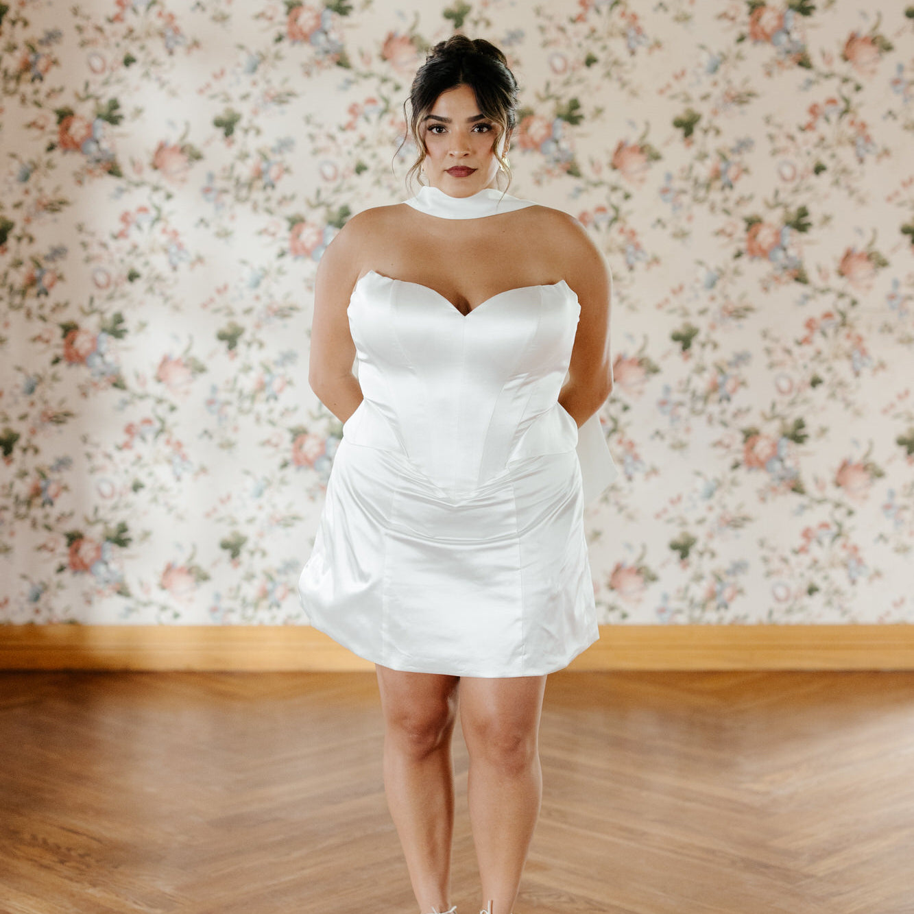 Woman wearing a white dress standing in front of floral wallpaper.