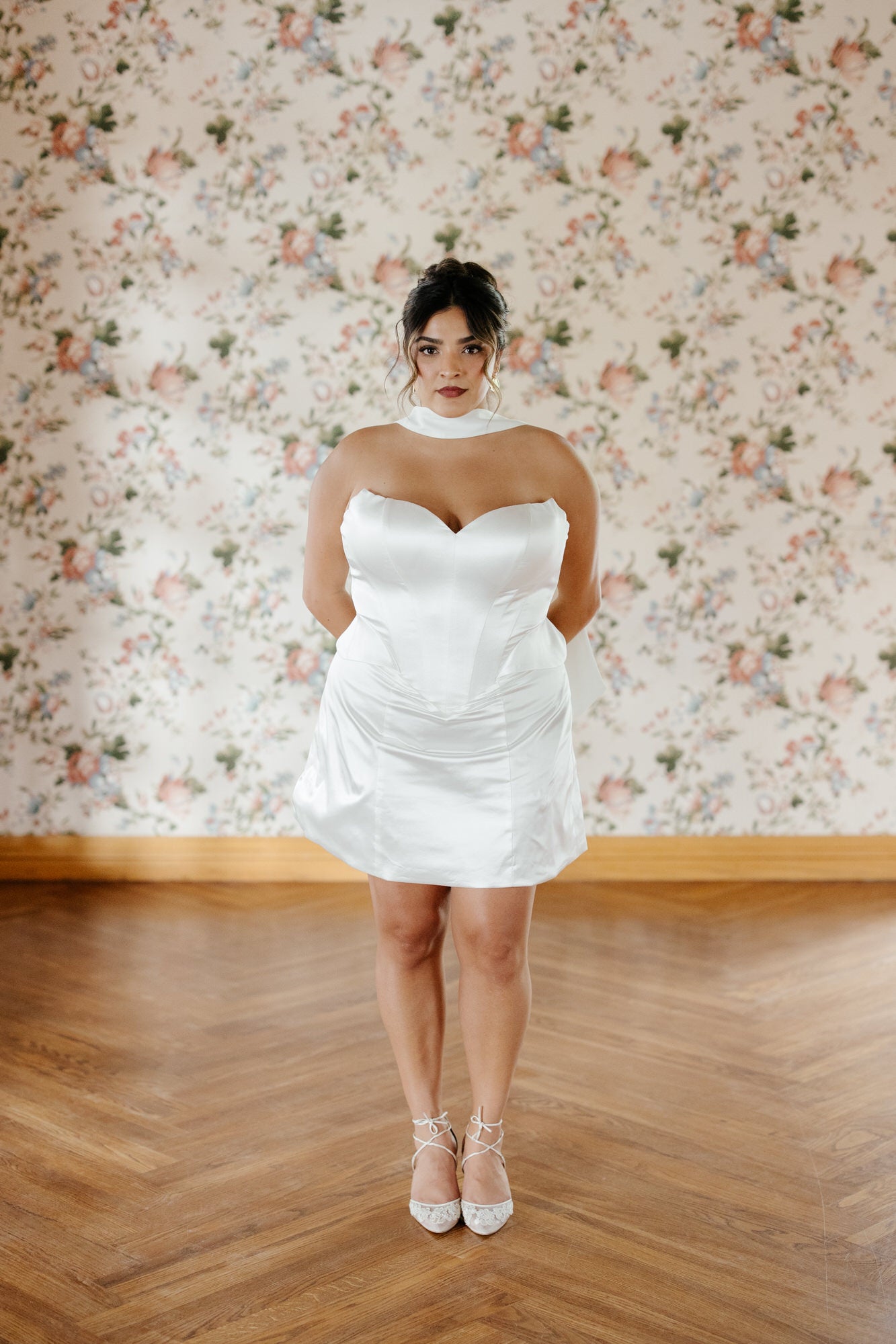 Woman wearing a white dress standing in front of floral wallpaper.