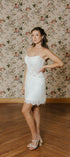 Woman in a white strapless dress standing against a floral wallpapered wall.
