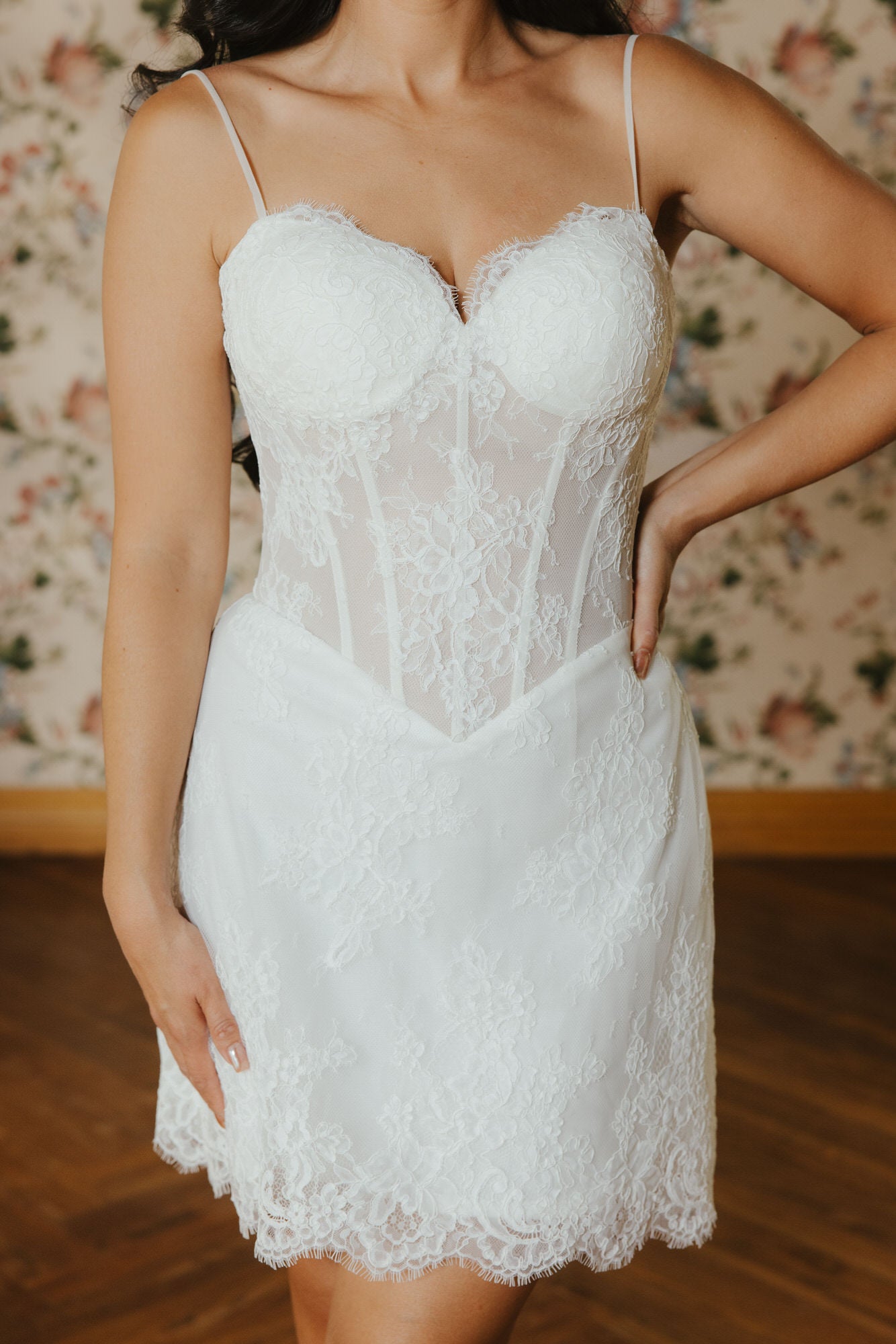White lace dress worn by a person with a floral wallpaper background