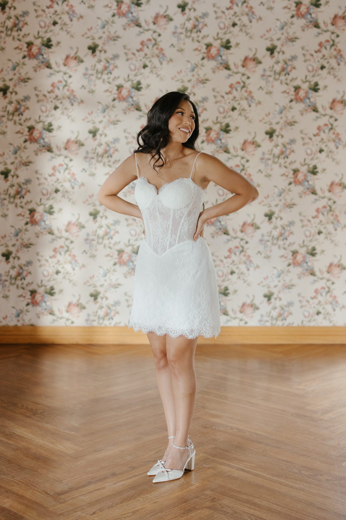 Woman in a white dress standing in front of floral wallpaper