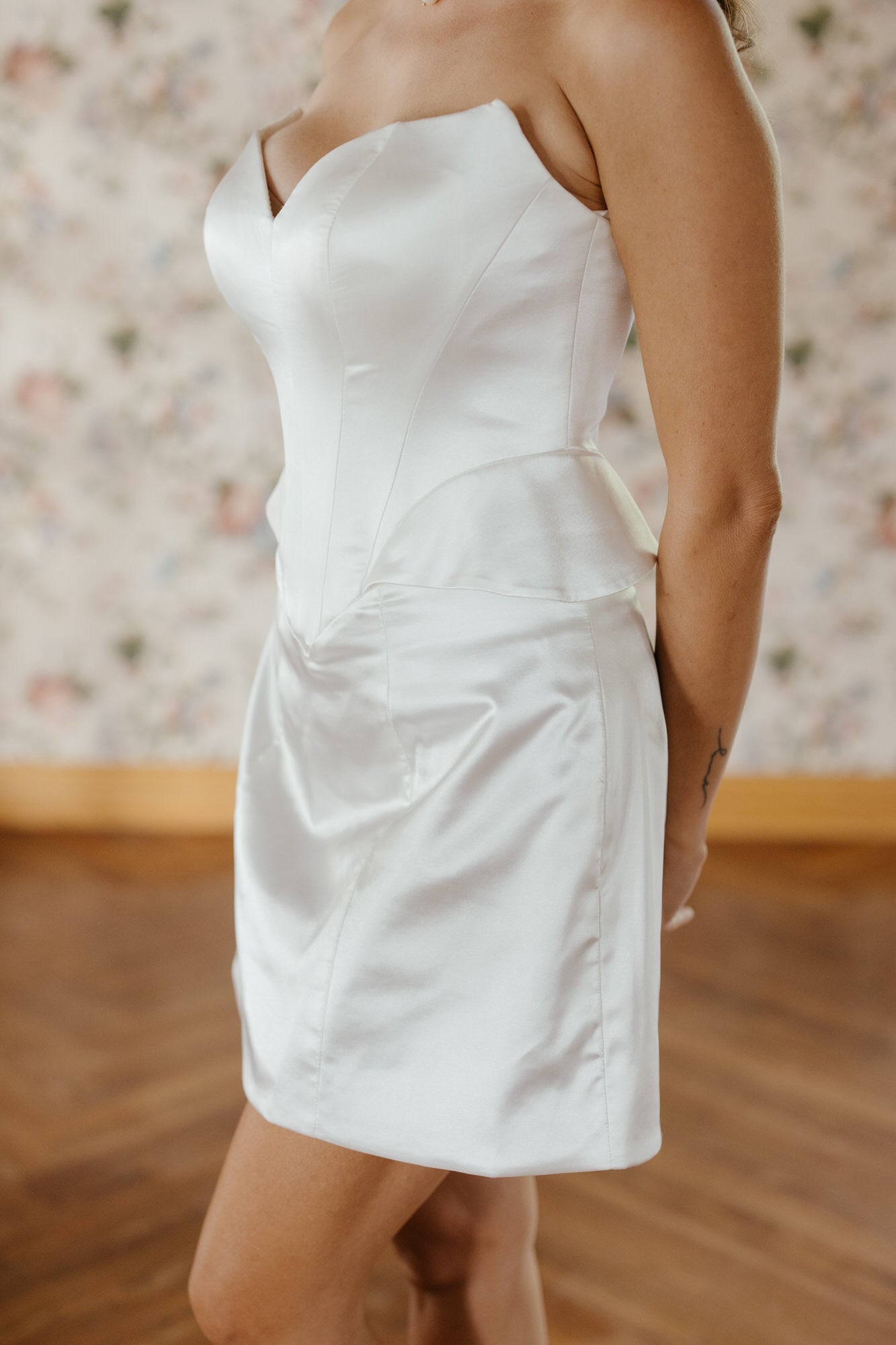White strapless dress worn by a person with a floral-patterned wall in the background