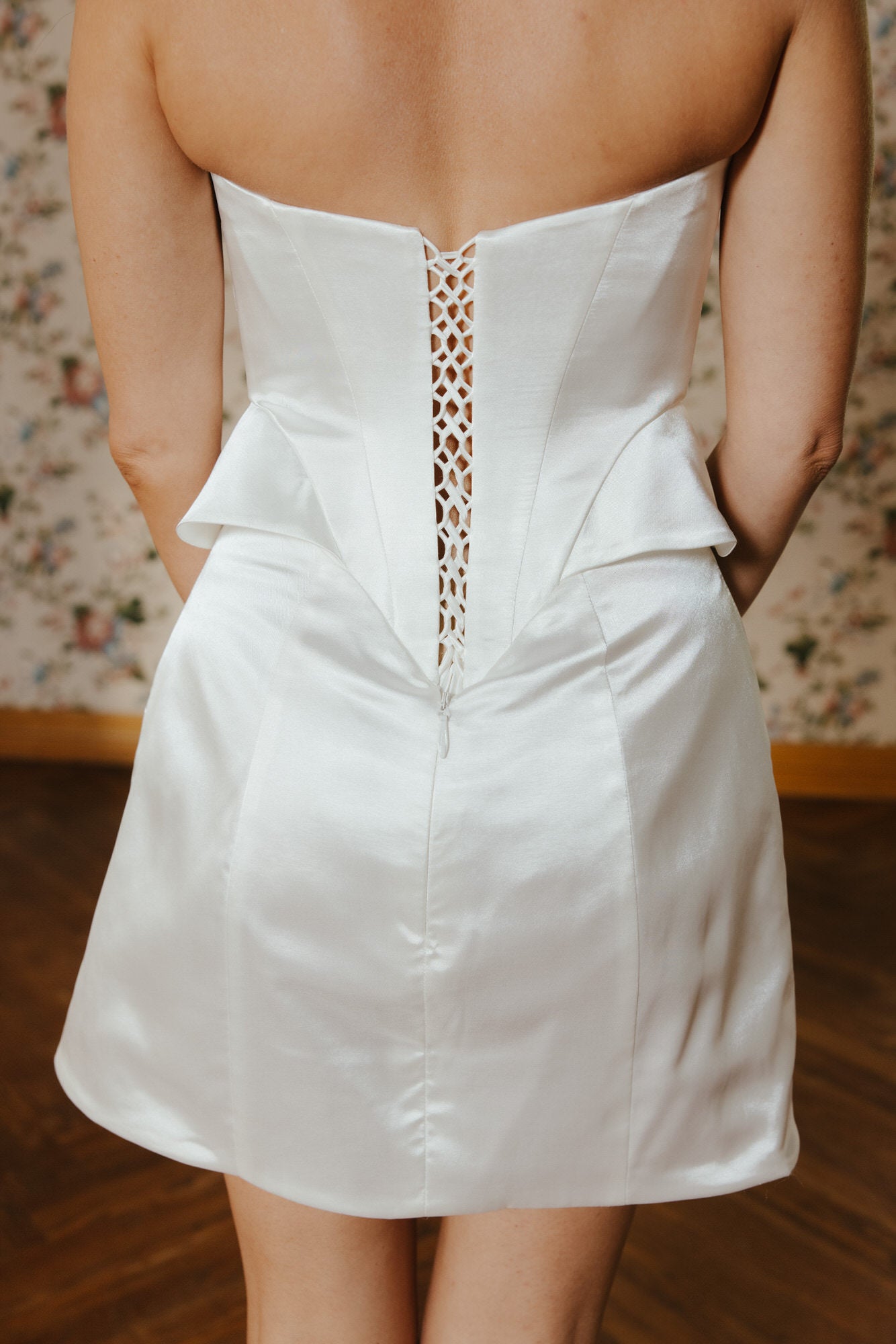 White strapless dress with lace detailing on a floral wallpaper background
